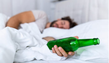 Мужчина лежит на кровати и держит бутылку